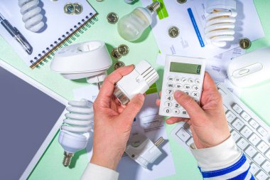 Modern modernleşme teknolojisi ve cihazlarıyla enerji tasarrufu. Elektrik faturaları, LED ampuller, ısı termostatı, açık yeşil masa fotokopi alanındaki hesap makinesi. Yeşil olsun, enerji maliyetleri kavramı