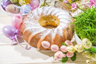 Geleneksel bahar bayramı pudra şekerli paskalya pastası. Hafif ahşap arka planda güneş ışığı, Paskalya yumurtaları, dekor ve bahar dalları