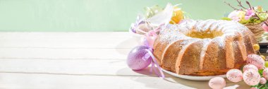 Geleneksel bahar bayramı pudra şekerli paskalya pastası. Hafif ahşap arka planda güneş ışığı, Paskalya yumurtaları, dekor ve bahar dalları