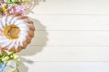 Geleneksel bahar bayramı pudra şekerli paskalya pastası. Hafif ahşap arka planda güneş ışığı, Paskalya yumurtaları, dekor ve bahar dalları