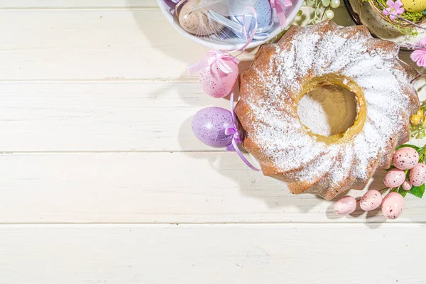 Geleneksel bahar bayramı pudra şekerli paskalya pastası. Hafif ahşap arka planda güneş ışığı, Paskalya yumurtaları, dekor ve bahar dalları