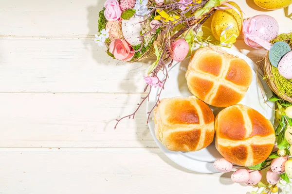 Traditional spring holiday Easter baking pastry  hot cross buns. On light wooden background with sunlight, Easter eggs, spring branches