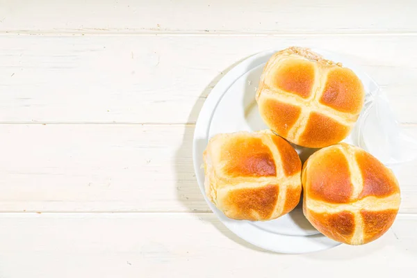 Traditional spring holiday Easter baking pastry  hot cross buns. On light wooden background with sunlight, Easter eggs, spring branches