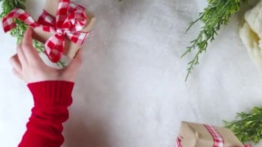 Kadın elleri yeni yıl hediyelerini süslüyor, el işi paketler şenlikli kurdeleler, beyaz kürk arka planda Noel ağacı dalları, düz bir üst görünüm