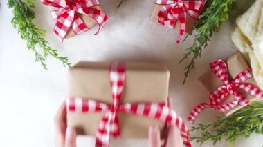 Kadın elleri yeni yıl hediyelerini süslüyor, el işi paketler şenlikli kurdeleler, beyaz kürk arka planda Noel ağacı dalları, düz bir üst görünüm