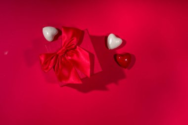 Sevgililer Günü tatili geçmişi. Kurdeleli el işi kağıt hediye kutusu, gül çiçekleri ve kalpler dekorasyonu, kırmızı arkaplan üst görünümü üzerinde kopyalama alanı