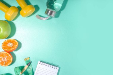 Bahar, yaz zayıflama mevsimi konsepti. Sulu spor şişesi, fitness dambılları, plaj şezlongu dekor, mezura, not defteri, elma, açık mavi arka planda dilimlenmiş turuncu. Düz kopya alanı üst görünümü