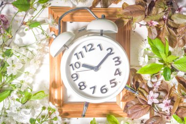 Bahar İleri Saati, Tasarruf Günışığı Konsepti Alarm Saati ve Bahar Bahçesi Çiçekleriyle ahşap arka planda düz kopya alanı ahşap beyaz arka planda