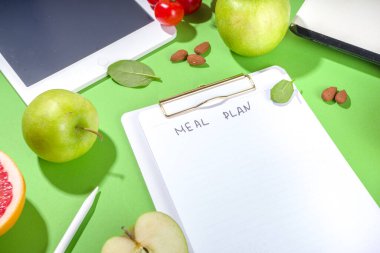 Yemek diyet planı konsepti, not defterinde, sağlıklı yiyecek meyveleri, sebzeler, tablet, not defterleri ve parlak yeşil masa arkaplanını sümüklendirmek için aksesuarlar ile