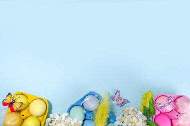 Preparation for Easter holiday concept with handcrafted painted colorful Easter eggs  blue, pink, yellow, with feather, spring blooming flowers and butterflies flatlay copy space