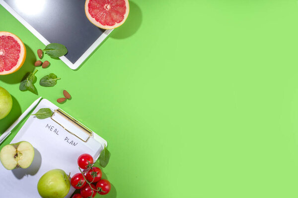Питание план концепции диеты, с в блокноте, здоровое питание фрукты, овощи, планшеты, ноутбуки и аксессуары для похудения на ярко-зеленом фоне стола