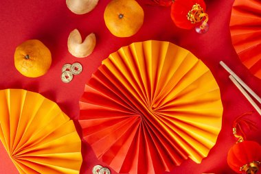 Çin 'in yeni yıl geçmişi. Geleneksel Çin Yeni Yıl dekoruna sahip kırmızı ve sarı düz yatak, dileklerle dolu zarflar, altın sikkeler, yelpazeler, Çin fenerleri, portakallar ve çay.