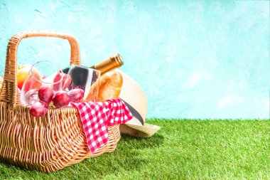 Piknik sepeti içinde yiyecek, şarap şişesi, bardaklar ve meyveler yeşil, güneşli çimlerde 