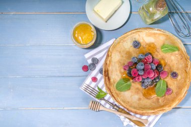 Rus Ukrayna Avrupa bayramı Maslenitsa. Geleneksel ince krep krepleri, böğürtlenli, reçelli ve bal soslu ahşap mavi masa, üst görünüm kopyalama alanı