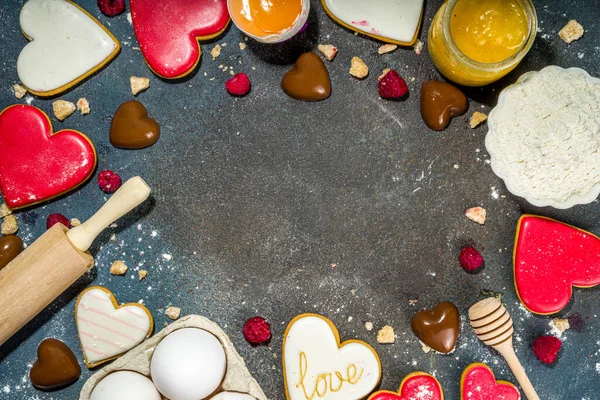 Valentine day sweet cooking background. Baking ingredients and utensils - flour, rolling pin, heart shaped biscuits, eggs. Making cute Valentine`s sweet gift. Top view copy space on dark blue background