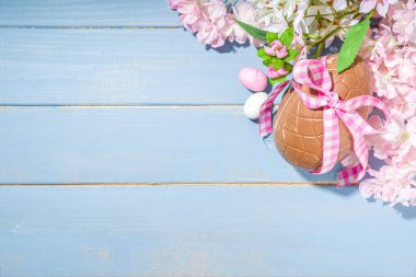 Paskalya bayramı tebrik kartı arka planı, çikolata yumurtaları ve çiçek açan bahar çiçekleri, açık mavi arka plan düz çerçeve fotokopi alanı üst görünümü