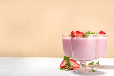 Ev yapımı tatlı çilekli panna cotta tatlı, pembe İtalyan panna cotta üç bardak, taze dilimlenmiş çilek ve naneli beyaz kaplama arka plan fotokopi alanı
