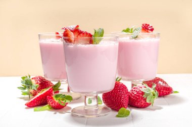 Ev yapımı tatlı çilekli panna cotta tatlı, pembe İtalyan panna cotta üç bardak, taze dilimlenmiş çilek ve naneli beyaz kaplama arka plan fotokopi alanı