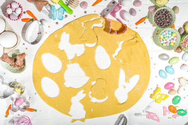 Женщина разминает тесто на столе и готовит пасхальное сахарное печенье. Пасхальный фон выпечки с красочными шоколадом, конфеты яйца, выпечки посуды, ингредиенты, вид сверху