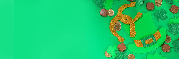 St Patrick flatlay background with shamrock clover leaves, leprechaun hat decor, golden coins and chocolates in form of symbol of st. patrician day