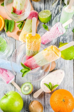 Renkli meyveli dondurma. Çubuklarda sulu dondurma lolipopları, farklı taze tropik meyveler, ahşap arka plan kopyalama alanı