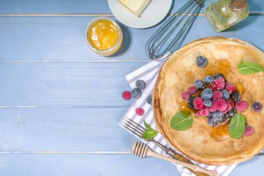 Rus Ukrayna Avrupa bayramı Maslenitsa. Geleneksel ince krep krepleri, böğürtlenli, reçelli ve bal soslu ahşap mavi masa, üst görünüm kopyalama alanı