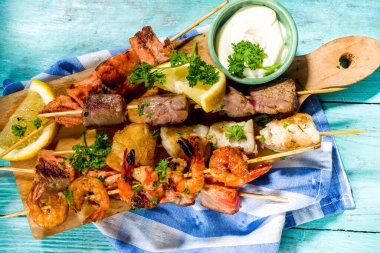 Çeşitli barbekü çeşitleri Akdeniz ızgara yiyeceği - balık, karides, yengeç, midye, soslu kebap, açık mavi güneşli ahşap arka plan