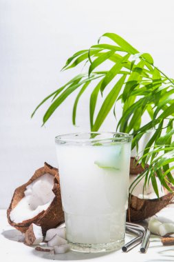 Yazın soğuk organik doğal içecek, bardakta taze hindistan cevizi suyu. Beyaz mermer bir arka planda tropik yapraklar ve taze hindistan cevizleri 
