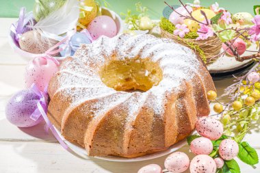 Geleneksel bahar bayramı pudra şekerli paskalya pastası. Hafif ahşap arka planda güneş ışığı, Paskalya yumurtaları, dekor ve bahar dalları