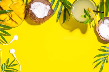 Şapkalı, mangolu, hindistancevizli, tropikal meyveli, palmiye yapraklı, kulaklıklı bir tropik yaz. Yaz tatili düzlüğü, tatil gezisi konsepti. Metin için en üst görünüm kopyalama alanı