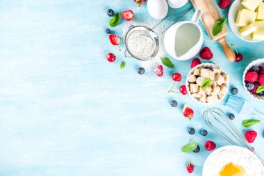 Böğürtlenli kek tarifi. Yaz pişirme arka planında çeşitli böğürtlenler, pişirme malzemeleri, aletler ve çatallar, açık mavi güneş ahşap arka planda düz bir zemin oluşturur.