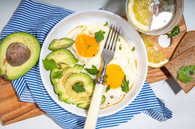 Sağlıklı kahvaltı. Keto, dengeli diyet. Dilimlenmiş avokadolu sahanda yumurta ve arka planda kızarmış ekmek. 