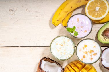 Yoğurt, milkshake ya da meyve suyu. Meyveli milkshake ile üç bardak. Beyaz muz, yeşil elma avokadosu, sarı mango tropikal meyve püresi. Beyaz ahşap masaya, boşluğu kopyala