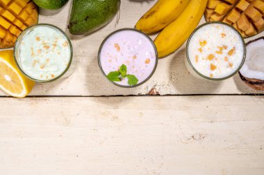 Yoğurt, milkshake ya da meyve suyu. Meyveli milkshake ile üç bardak. Beyaz muz, yeşil elma avokadosu, sarı mango tropikal meyve püresi. Beyaz ahşap masaya, boşluğu kopyala