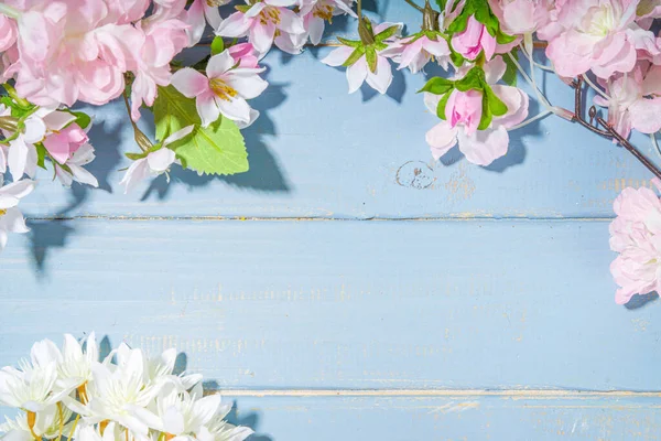Merhaba bahar konsepti. Bahar tatili tebrik kartı suni çiçekli sade yassı arka plan açık mavi ahşap bahçe masası arkaplan çerçeve fotokopi alanı üst görünüm