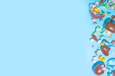 Mutlu Paskalya Renkli Düzüşmeler. Mavi arka planda bayram kurdelesi olan parlak renkli ve çikolatalı Paskalya yumurtaları. Paskalya için tanıtım ve alışveriş şablonu