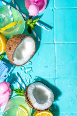 Parlak güneşli yaz tatili. Plaj tatil aksesuarları, flamingo cankurtaran şamandıraları, limonlar, hindistan cevizi, nane, tropikal yapraklar, düz üst görünüm kopya alanı ile arka planda limonata içilir.