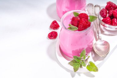 Taze ahududu ve Melissa nane yapraklı ahududu panna cotta tatlısı. Beyaz arka planda küçük porsiyon kavanozlarda pembe panna cotta