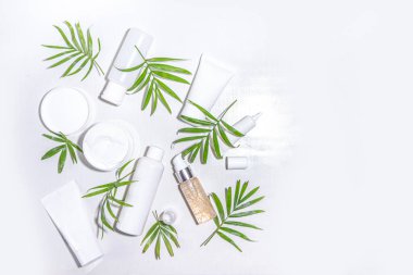 Beyaz zemin üzerinde tropikal palmiye yaprakları düz kopya alanı olan güzellik kozmetik ürünleri. Beyaz kavanozlar, tüpler, damlalar ve şişeler. Yaz kaplıcası, günlük doğal cilt bakımı rutin konsepti
