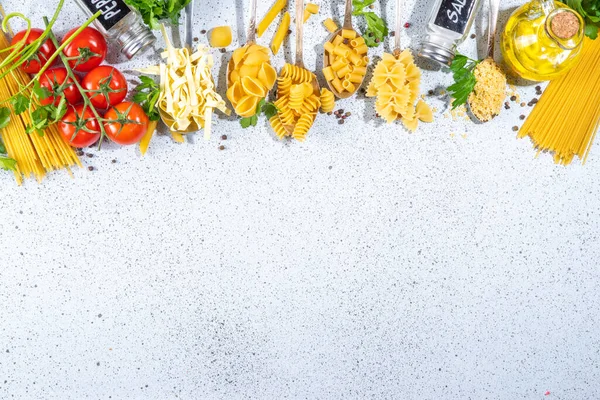 Beyaz masa arkasında çeşitli kurutulmuş spagetti, makarna ve kaşıklarla hazırlanmış makarna. Farklı şekillerde çiğ İtalyan makarnası, otlar, zeytinyağı, domatesler, baharatlar.