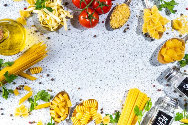 Beyaz masa arkasında çeşitli kurutulmuş spagetti, makarna ve kaşıklarla hazırlanmış makarna. Farklı şekillerde çiğ İtalyan makarnası, otlar, zeytinyağı, domatesler, baharatlar.