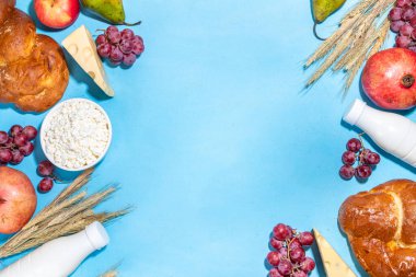 Yahudi bayramının sembolleri olan mutlu Shavuot tebrik kartı - nar, üzüm, elma, tatlı challah ekmeği, buğday filizi, süt, peynir, süzme peynir, açık mavi zemin