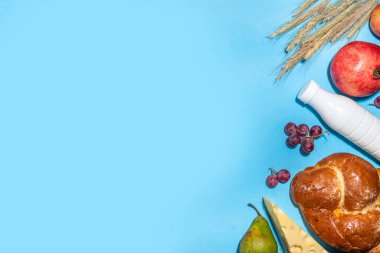 Yahudi bayramının sembolleri olan mutlu Shavuot tebrik kartı - nar, üzüm, elma, tatlı challah ekmeği, buğday filizi, süt, peynir, süzme peynir, açık mavi zemin