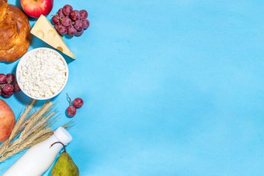 Yahudi bayramının sembolleri olan mutlu Shavuot tebrik kartı - nar, üzüm, elma, tatlı challah ekmeği, buğday filizi, süt, peynir, süzme peynir, açık mavi zemin