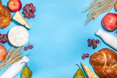 Yahudi bayramının sembolleri olan mutlu Shavuot tebrik kartı - nar, üzüm, elma, tatlı challah ekmeği, buğday filizi, süt, peynir, süzme peynir, açık mavi zemin