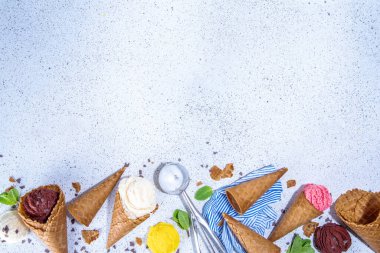 Waffle külahlarında parlak renkli dondurma koleksiyonu, beyaz beton arka planda çeşitli aromalı dondurma seti