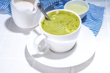 Beyaz beton arka planda kibrit yeşil çay, sert ışık, bir fincan kibrit içeceği kadınların elinde, üst görünüm kopya alanı 