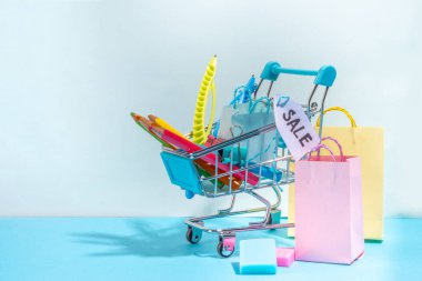 School sale concept. Shopping supermarket cart with colorful paper bags, school education supplies and accessories. Back to school shopping background, copy space