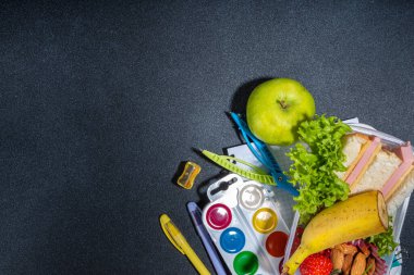 Sağlıklı okul beslenme çantası: sandviç, sebze, meyve, fındık ve yoğurt, okul çocukları için gerekli malzemeler, aksesuarlar ve siyah arka plan fotokopi alanı üzerine sırt çantası. Okul konseptine dönelim.