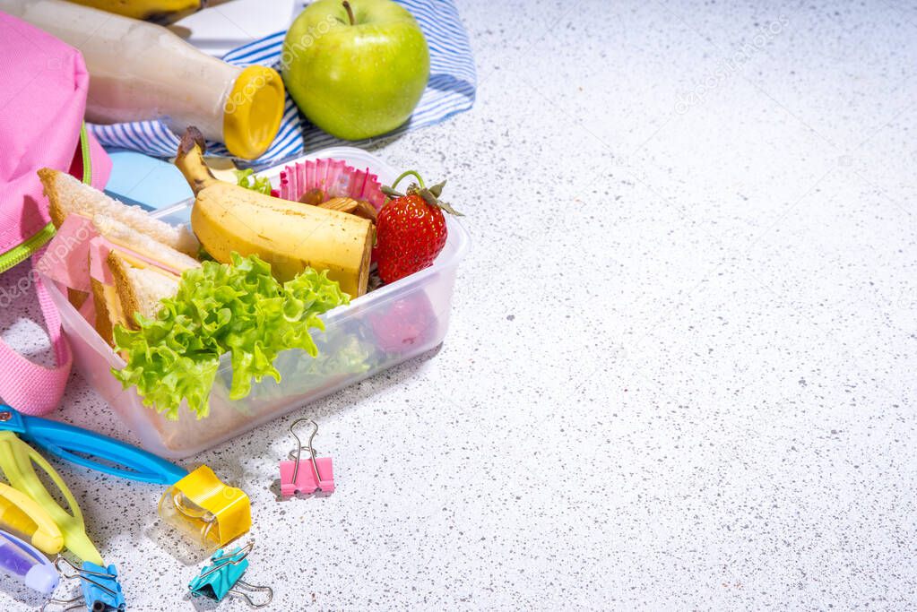 Healthy school lunch box: sandwich, vegetables, fruit, nuts and yogurt with school kids supplies, accessories and backpack on black background flatlay copy space. Back to school concept